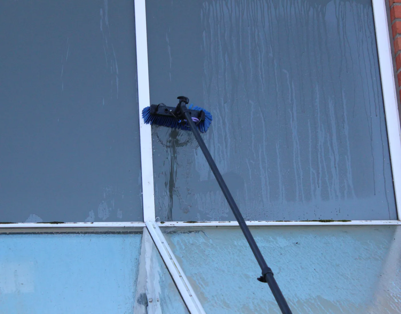 Eine Teleskopbürste von G&W reinigt eine große Glasfront.