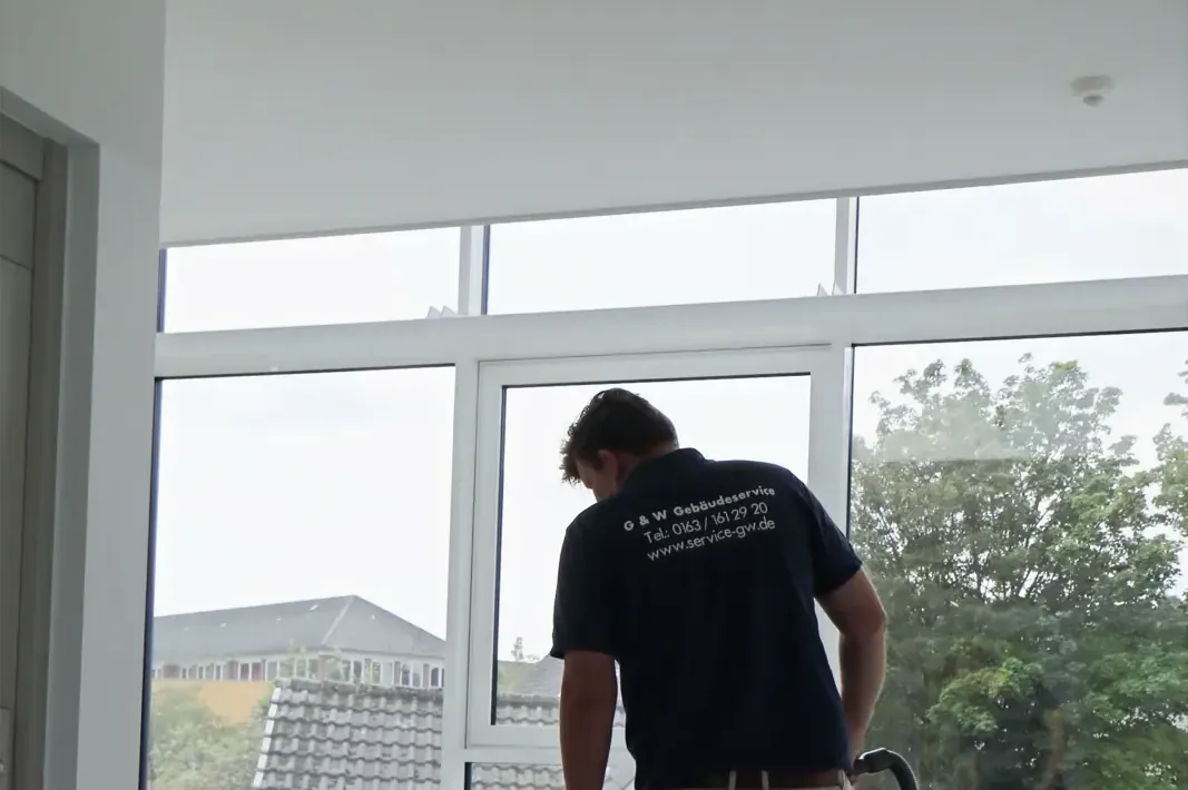 Ein Mitarbeiter von G&W im Firmenshirt reinigt den Boden eines hellen Flurs.